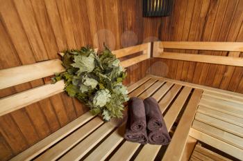Sauna for relaxation and spa therapy, towel on the wooden bench and broom on the background.