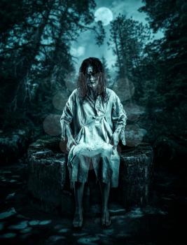 Scary corpse sitting on the well in the night forest. Halloween.