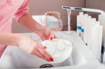 Doctor holding in a hand a cosmetic bowl of water filling from the faucet.