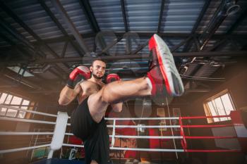 Strength  fighter in red boxing gloves at a training. Exercise for legs. Boxing ring on the background.