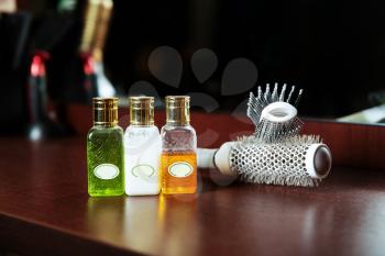Haircare balms in flask and hairbrush are located on a wooden table, hairdressing tools on the background.
