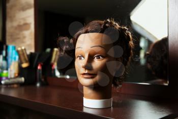 Female hairdressing mannequin is located on a wooden table, hairdressing tools on the background.