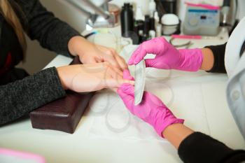 Manicure specialist in rubber gloves works with nailfile. Beauty salon.