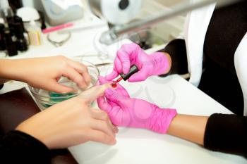 Manicurist in rubber gloves applies a lok on nails. Professional manicure tool.