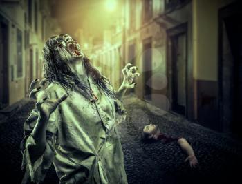 The horror shouting zombie girl on the dark street, bloody hand and head on the background. Vampire. Halloween.