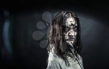 Portrait of the horror zombie woman with bloody face against the black background. Halloween. Scary.