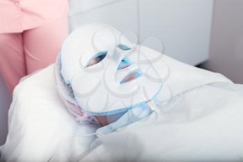 Woman in the light mask lying on a couch in a beauty salon