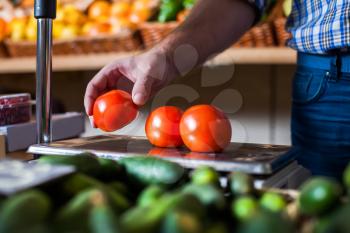 Male hand holding a tomato over the weights. Ecological food. Grocery on the background.