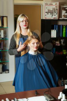 Professional hairdresser with beautiful woman in front of the mirror in hairdressing salon.