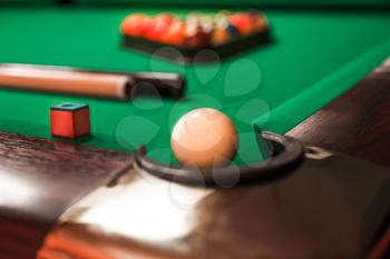 White billiard ball opposite to a pocket. Cue and triangle with balls on the background.