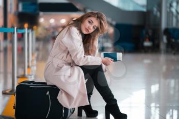 Young girl sits on a suitcase and holds the passport and the ticket in hand. Airport at the background. Tralev concept.