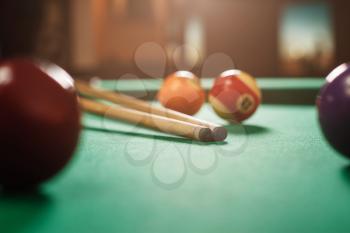 Two cues and spheres on green cloth of a billiard table. Nightlife.