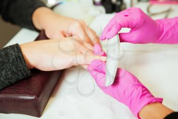 Manicure specialist in rubber gloves works with nailfile. Beauty salon.
