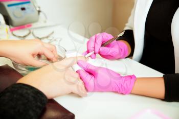Manicure specialist in rubber gloves care by finger nail in spa beauty salon. Manicurist uses professional manicure tool. Manicure service.