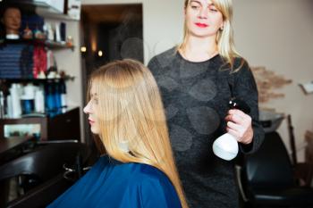 Professional woman hairdresser uses spray for hair at beauty salon.