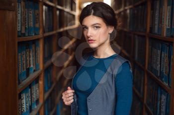 Female student standing between bookshelves in library. 