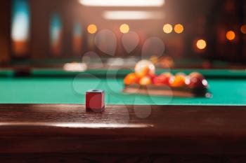 Chalk on the wooden edge of the billiard table. Balls in a pool triangle on the background.