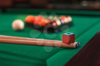 Cues and chalk on a pool table. Billiard balls in triangle on the background.
