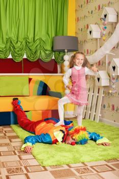 Smiling little girl has won a game against the clown. Decorated kindergarten on the background