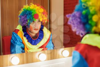Circus clown looks in a mirror in a make-up room. In waiting of the entertainment.
