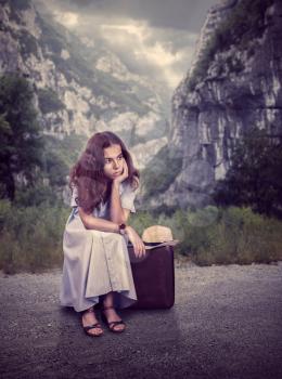 Young woman sitting on her suitcase with rocky mountains landscape on the background. Retro style concept.
