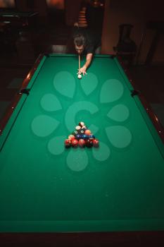 Player prepares to breaks a pyramid in billiards. Nightlife. Billiard room on the background. Above view.