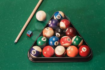 Billiard balls in triangle near by cue and chalk on the pool table.