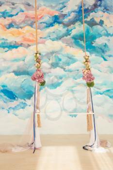White wooden swing decorated with bouquets of flowers agaist abstract watercolor background. Romantic wedding concept.