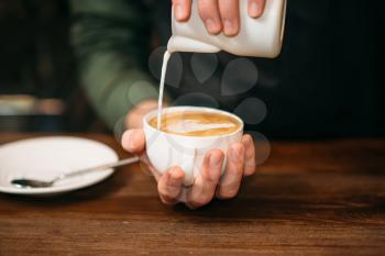 Closeup of male hands adding cream to coffee. Blur table, plate and spoon on the background.