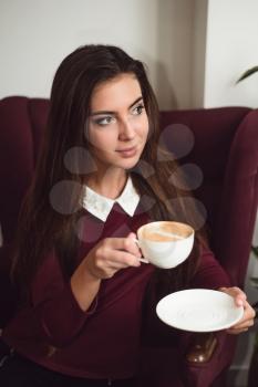 Young woman sitting in a red armchair and drinking fresh coffee.