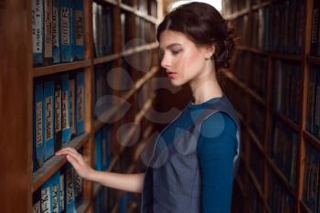 Young woman selecting book from library shelf. Knowledge, education and studying concept.