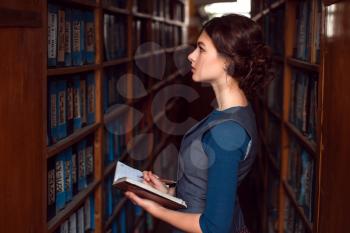 Young girl with notebook select textbook in college library.
