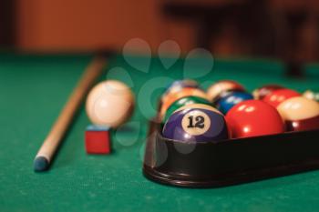 Billiard balls in triangle near by cue and chalk on the pool table.