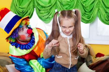 Smiling child girl and clown with colourful cap playing on birthday party. Clown in rainbow colors costume.