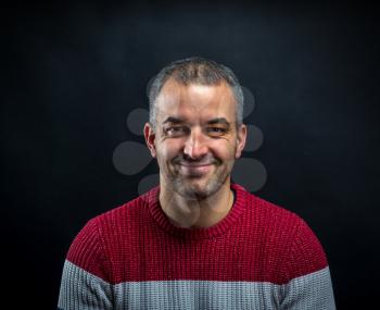 Portrait of smiling man in pullover isolated on black background. Brutal unshaven handsome man in professional studio.