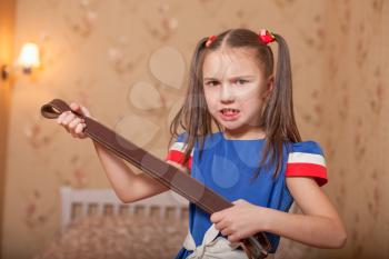 Angry little girl with belt in hand. Bedroom on the background.