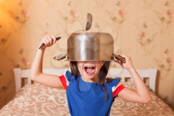 Female child fool around with pan and serving spoon on head.