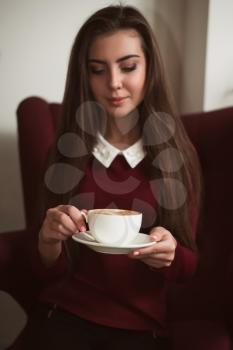 Young woman sitting in a red armchair and drinking fresh coffee