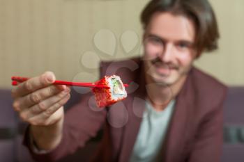 Man hold chopsticks in hand. Chopsticks with sushi roll. 