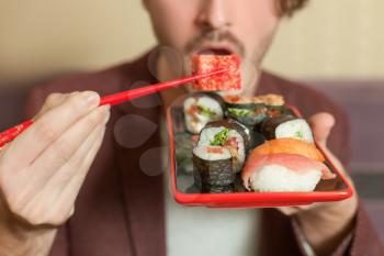 Man hold chopsticks in hand. Chopsticks with sushi roll.