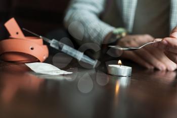 Addict with candle and spoon preparing dose of narcotic closeup.