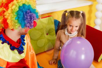 Amusing clown give air balloon to the little girl. Clown in colorful costume on birthday party.