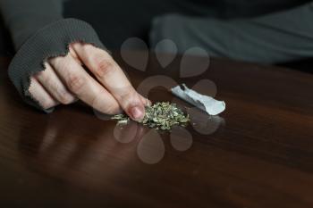 Addict hands making marijuana jamb closeup, wooden background.