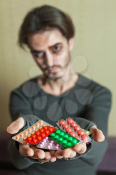 Drugs addict is holding a lot of different tablets in both his hands.