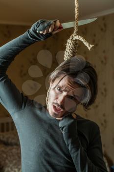 Depressed man with a noose around his neck trying to cut rope with knife.