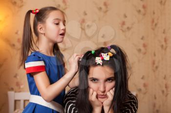 Little kid making hairstyle to her young mother.