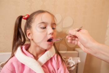 Little girl drinks mixture from a spoon. Child illness concept.