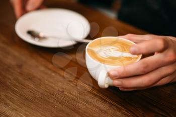 Man hands holding a cup of coffee with cream, blur background.