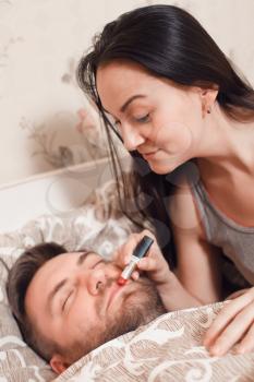 Playful woman makes up the man's lips with lipstick while he sleeps.