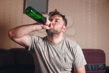 Hangover after hard drinking. Alcohol addicted man with bottle.